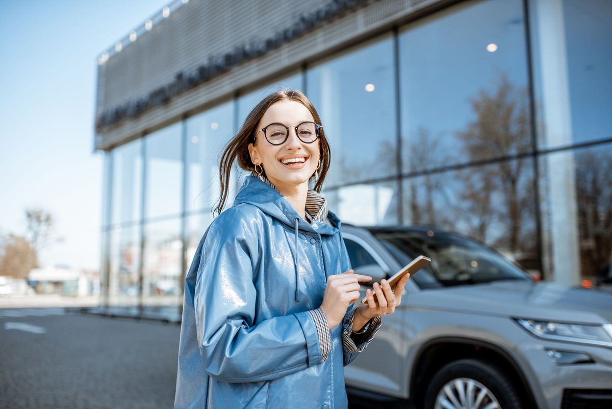 Ondernemer met smartphone voor haar nieuwe auto bij de dealer